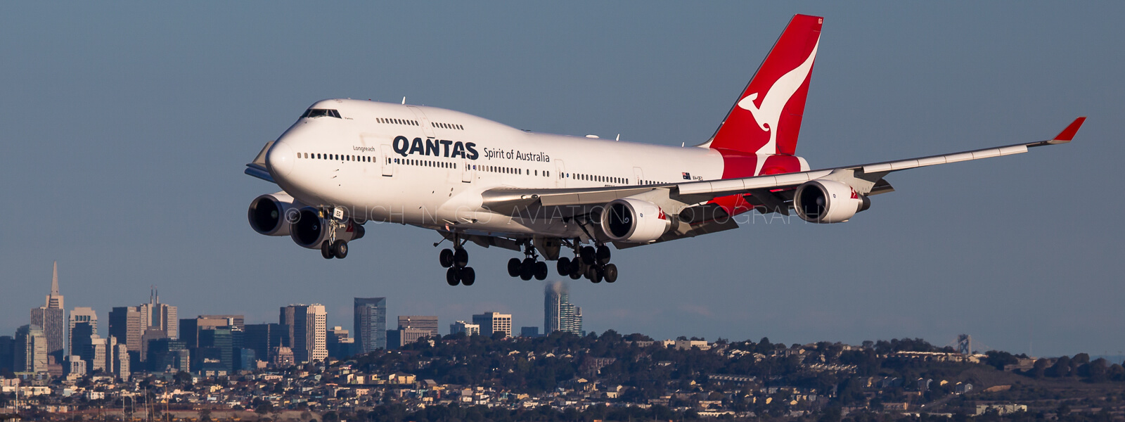 Quantas 747 arriving into SFO with San Francisco cityscape in the background.