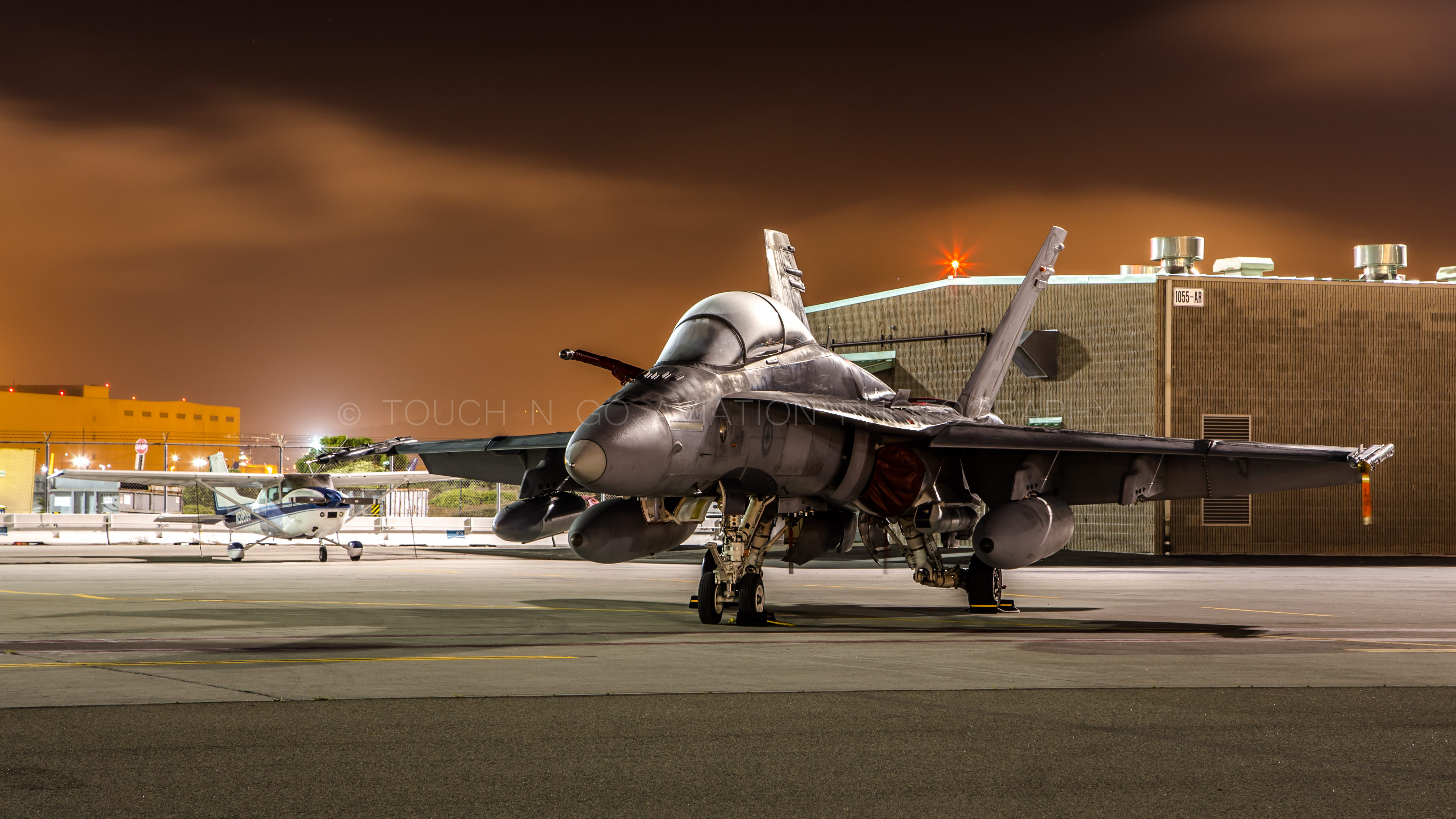 Night shot of a tiny cessna parked next to a CF 18, SFO.