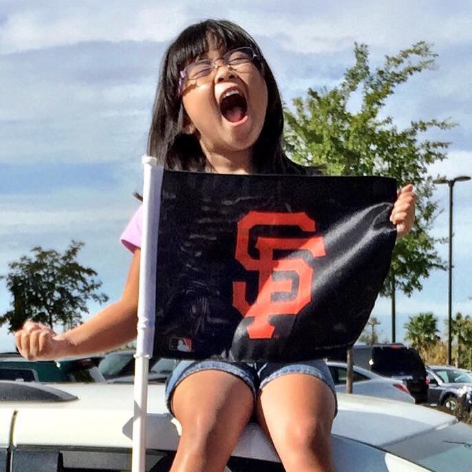 Rhiannon sitting on top of the car screaming joyously while holding an SF Giants flag